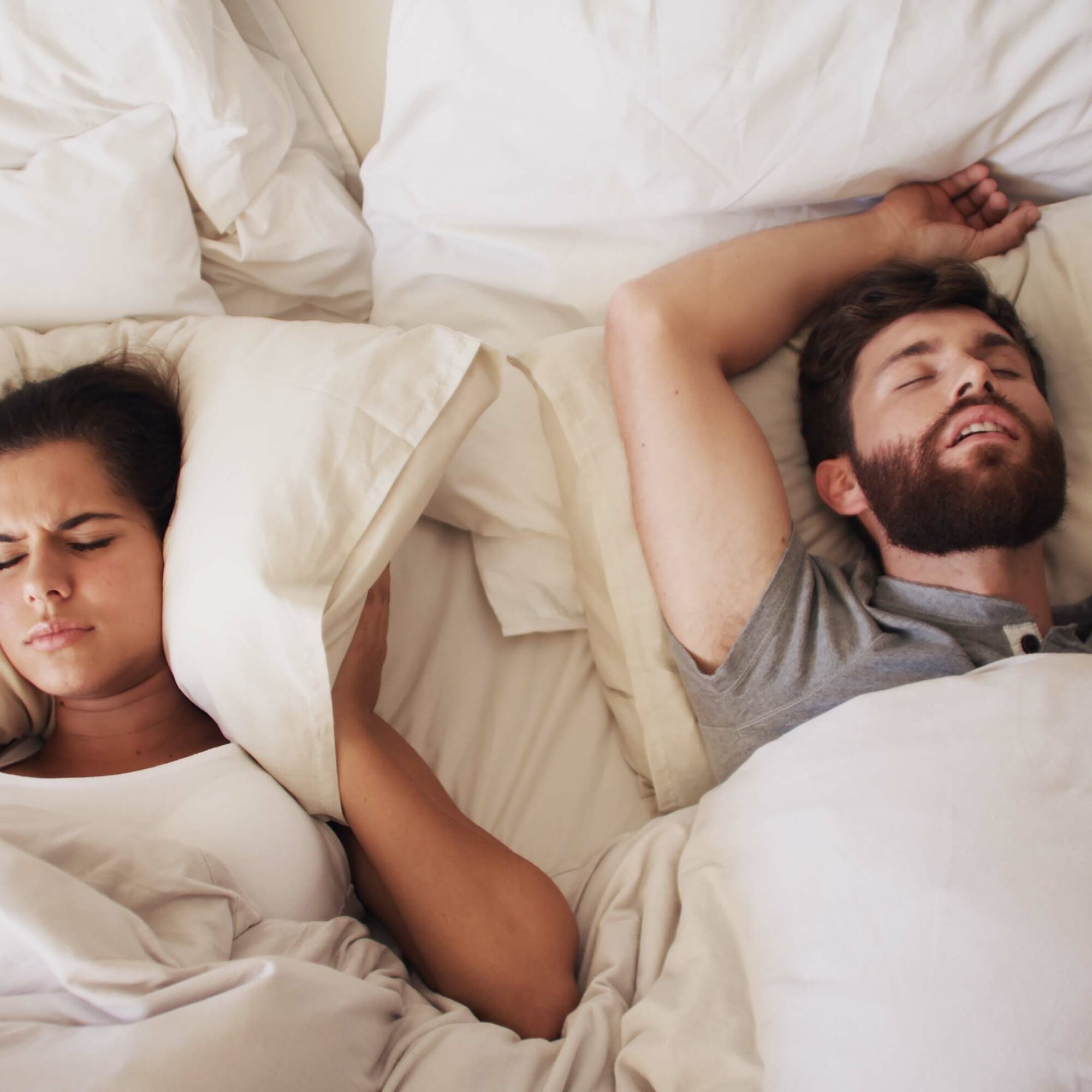 man in woman in bed, woman covering her ears from husbands snoring